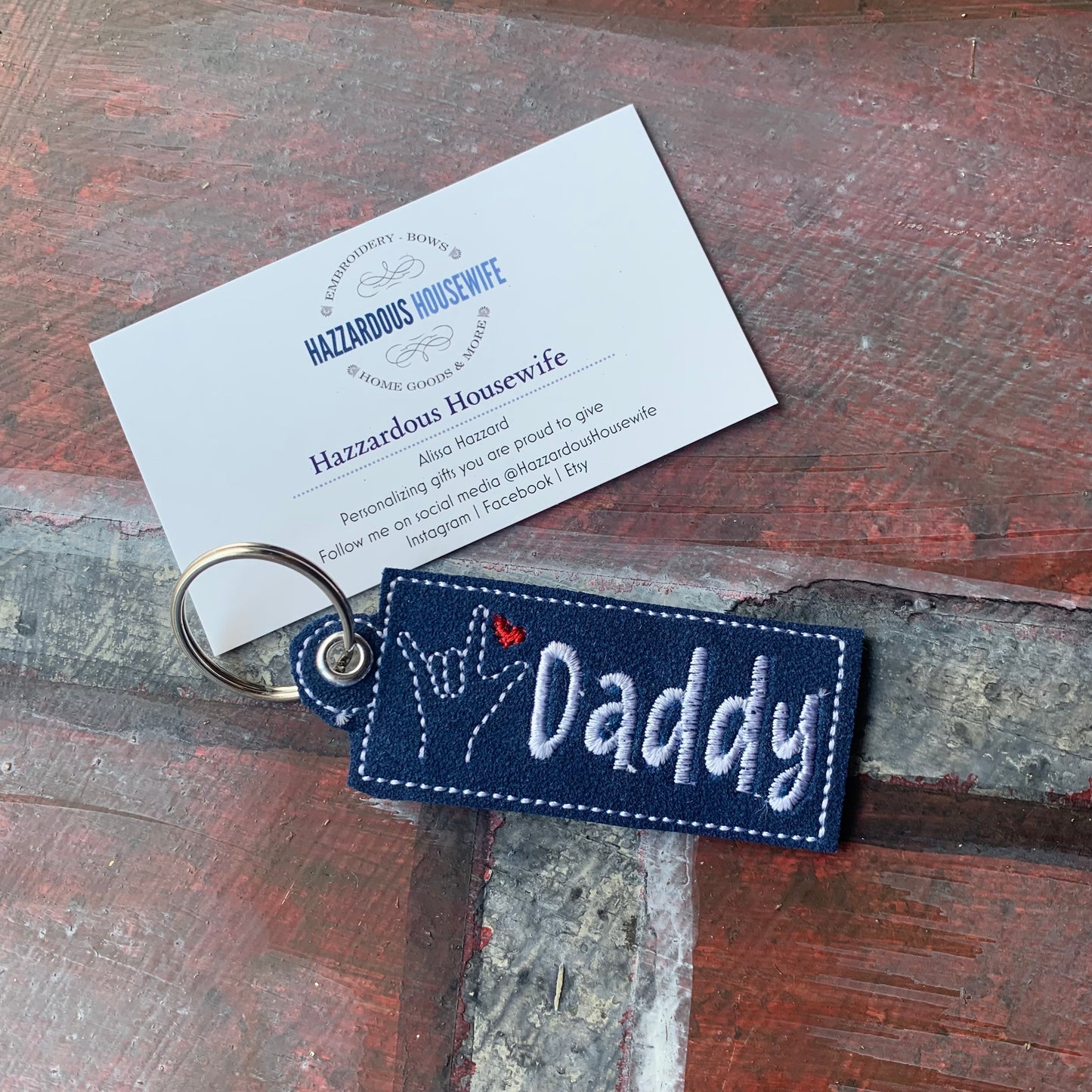Navy blue keychain with 'Daddy' text on a wooden surface with a business card.