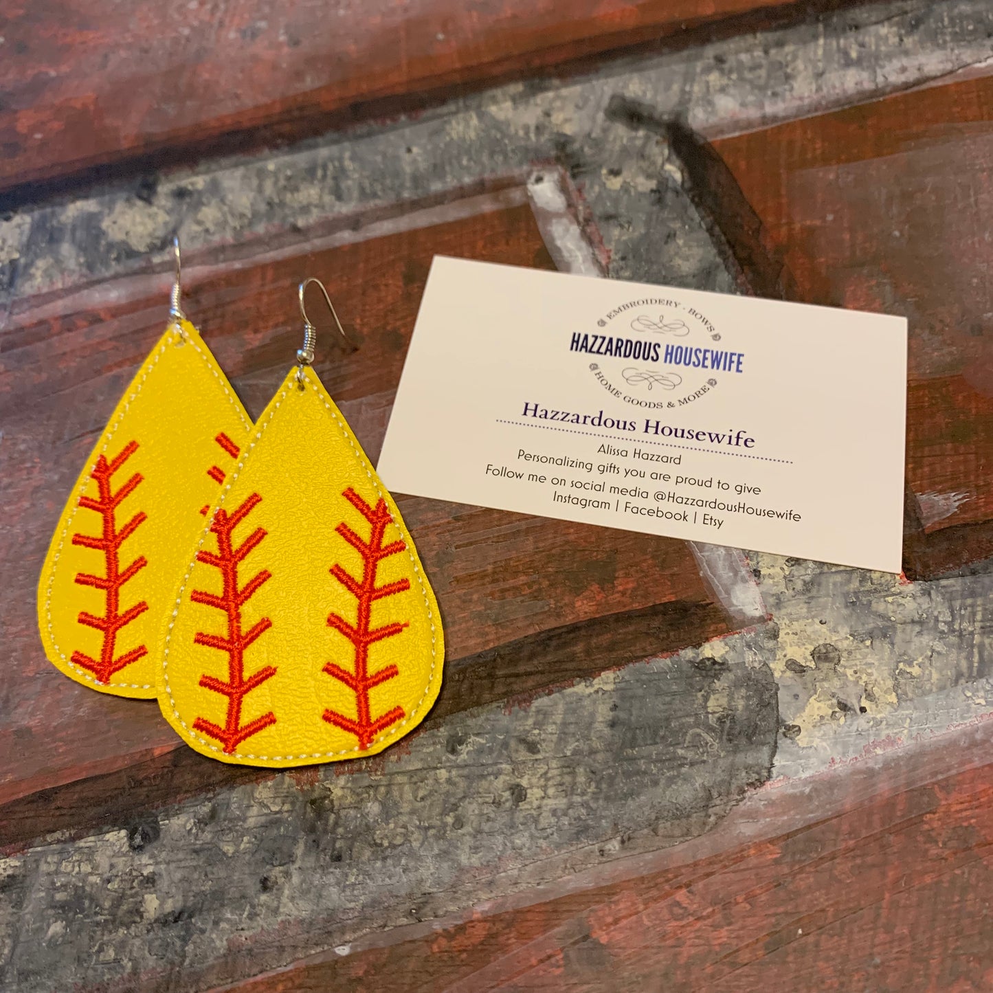 Yellow earrings with red stitching on a wooden surface with a HazzardousHousewife business card.