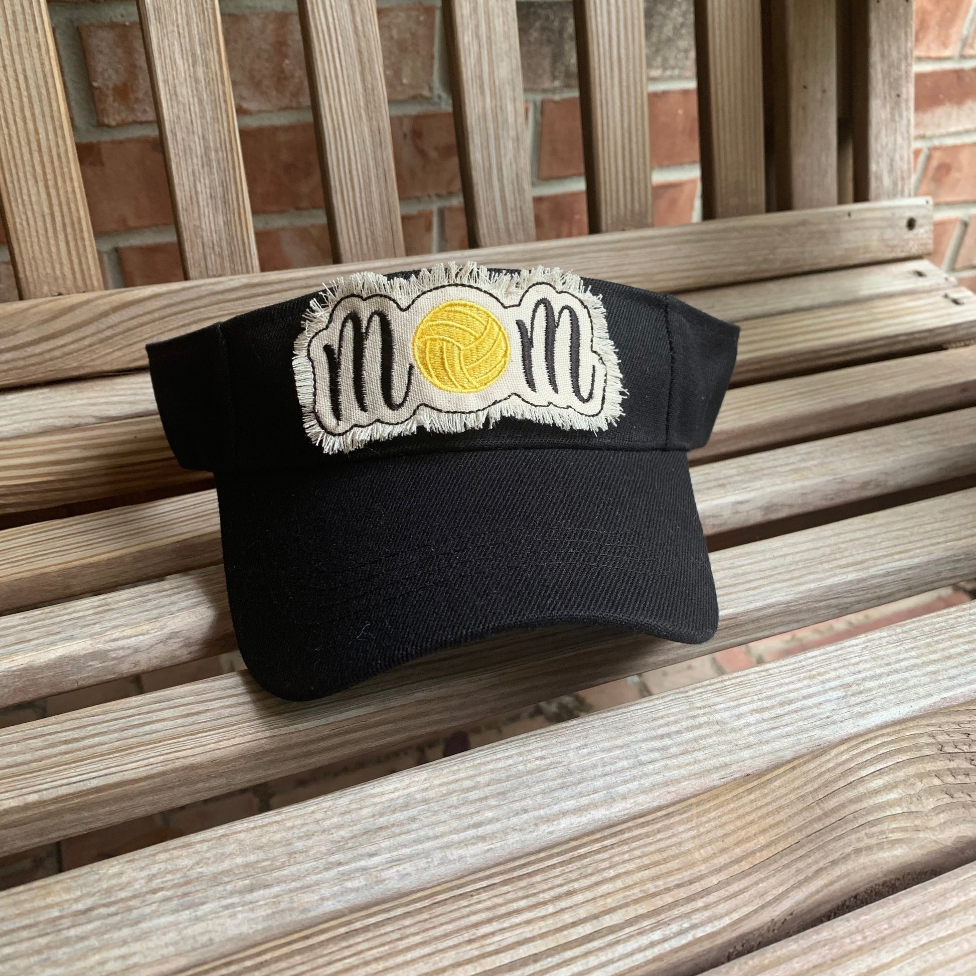 Black cap with 'mom' and water polo design on a wooden bench