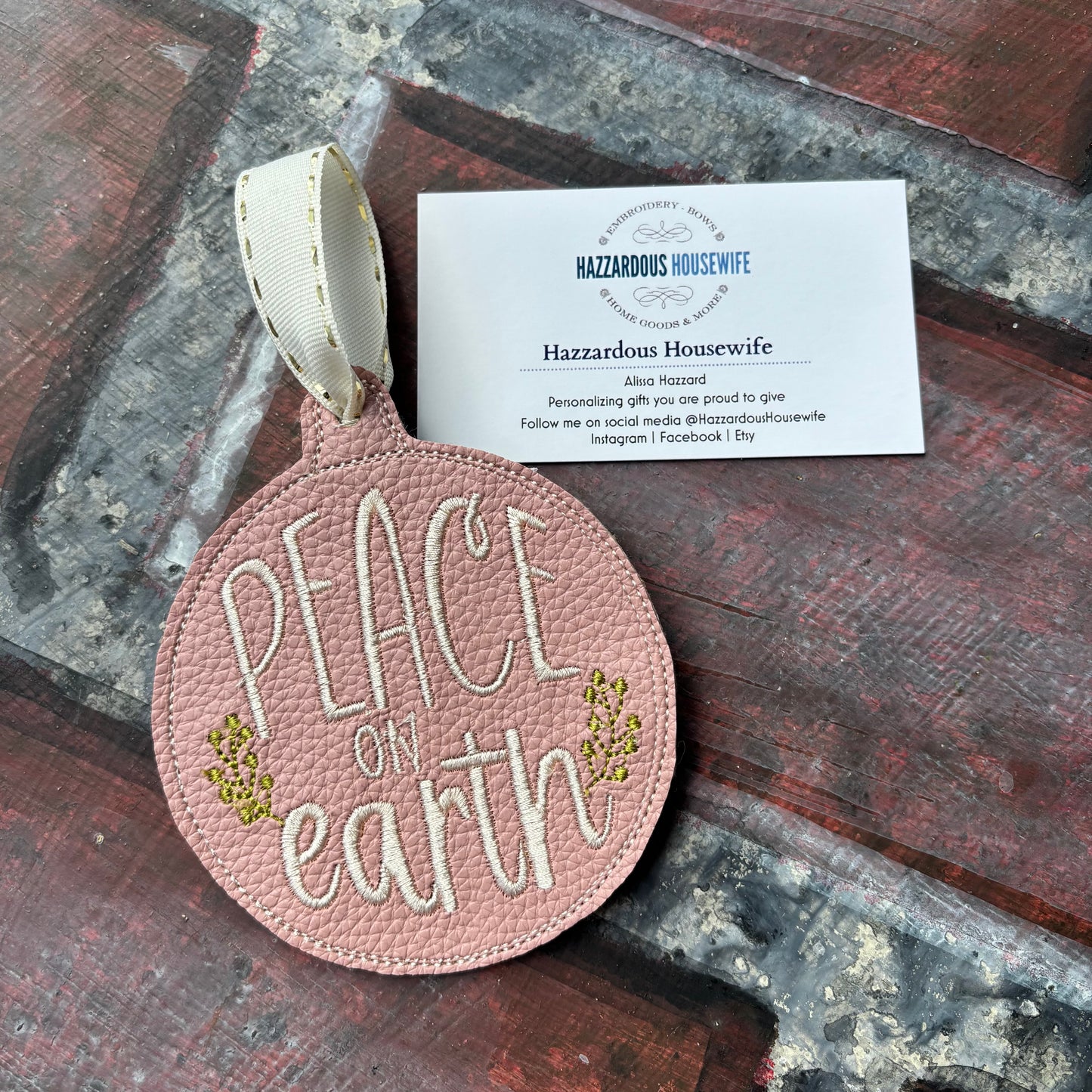 Round pink leather tag with 'Peace on Earth' text and ribbon, placed on a textured surface.