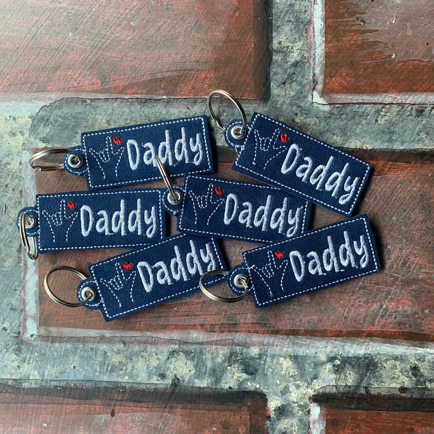 Set of blue 'Daddy' keychains on a rustic wooden surface