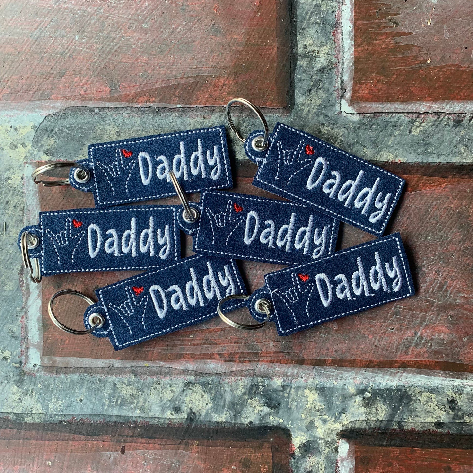 Set of blue 'Daddy' keychains on a rustic wooden surface