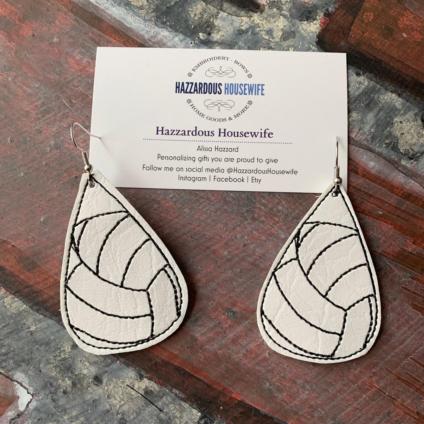 Teardrop-shaped volleyball earrings with a pattern on a card displaying 'Hazzardous Housewife' brand.
