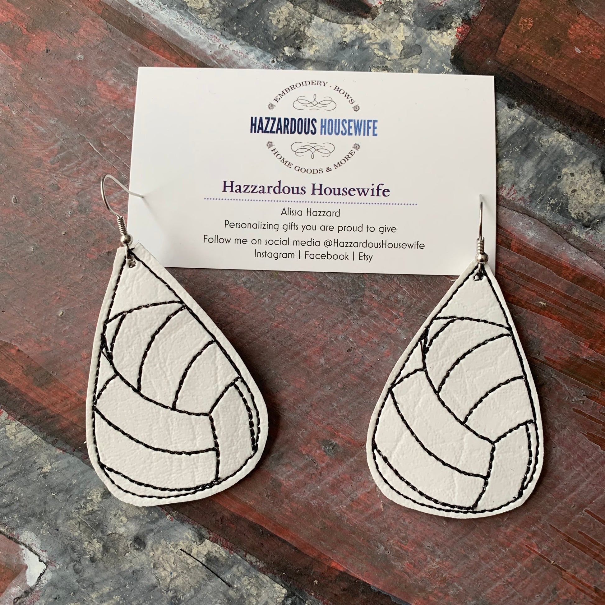 Teardrop-shaped volleyball earrings with a pattern on a card displaying 'Hazzardous Housewife' brand.