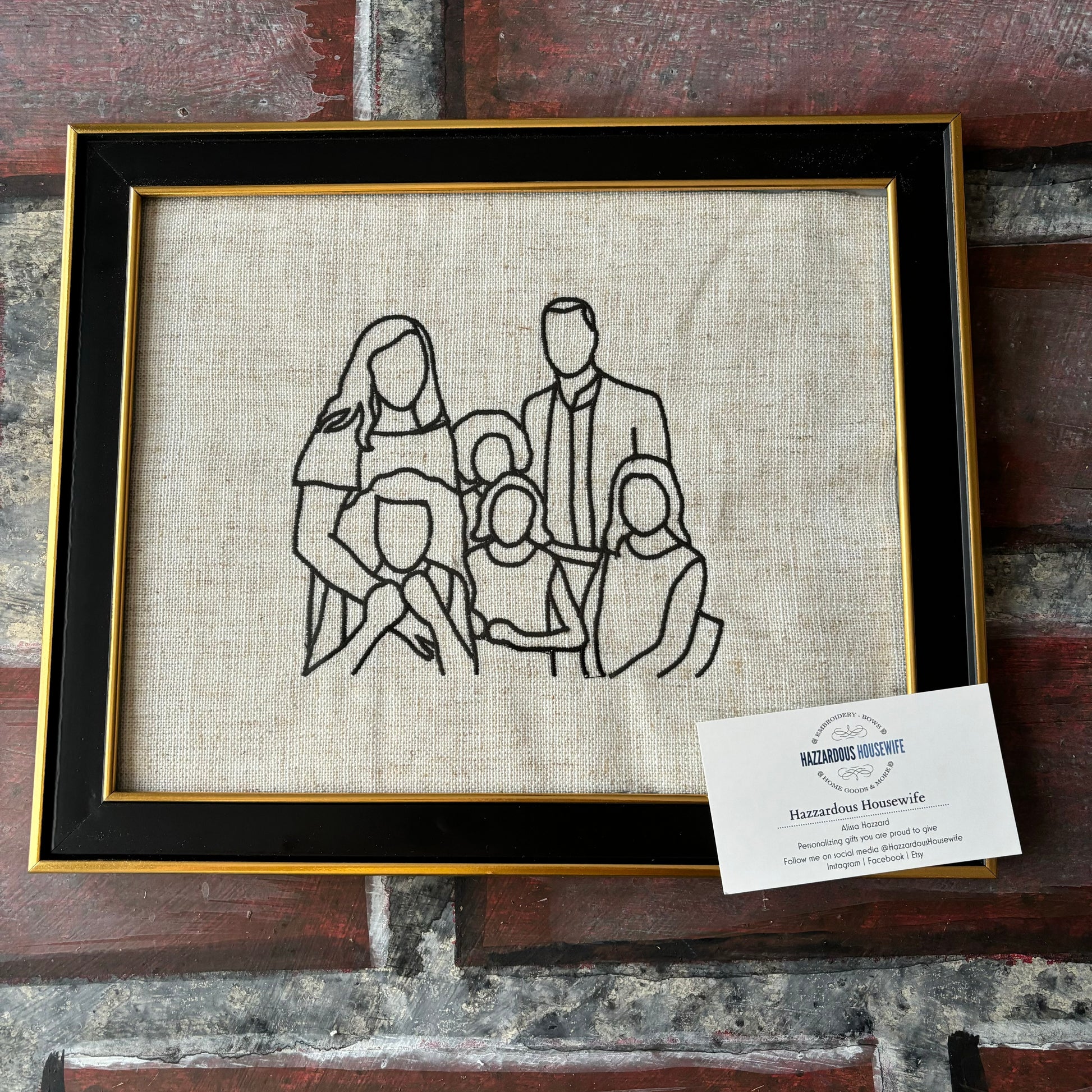 Framed black line drawing of a family on a textured fabric background with a card below.