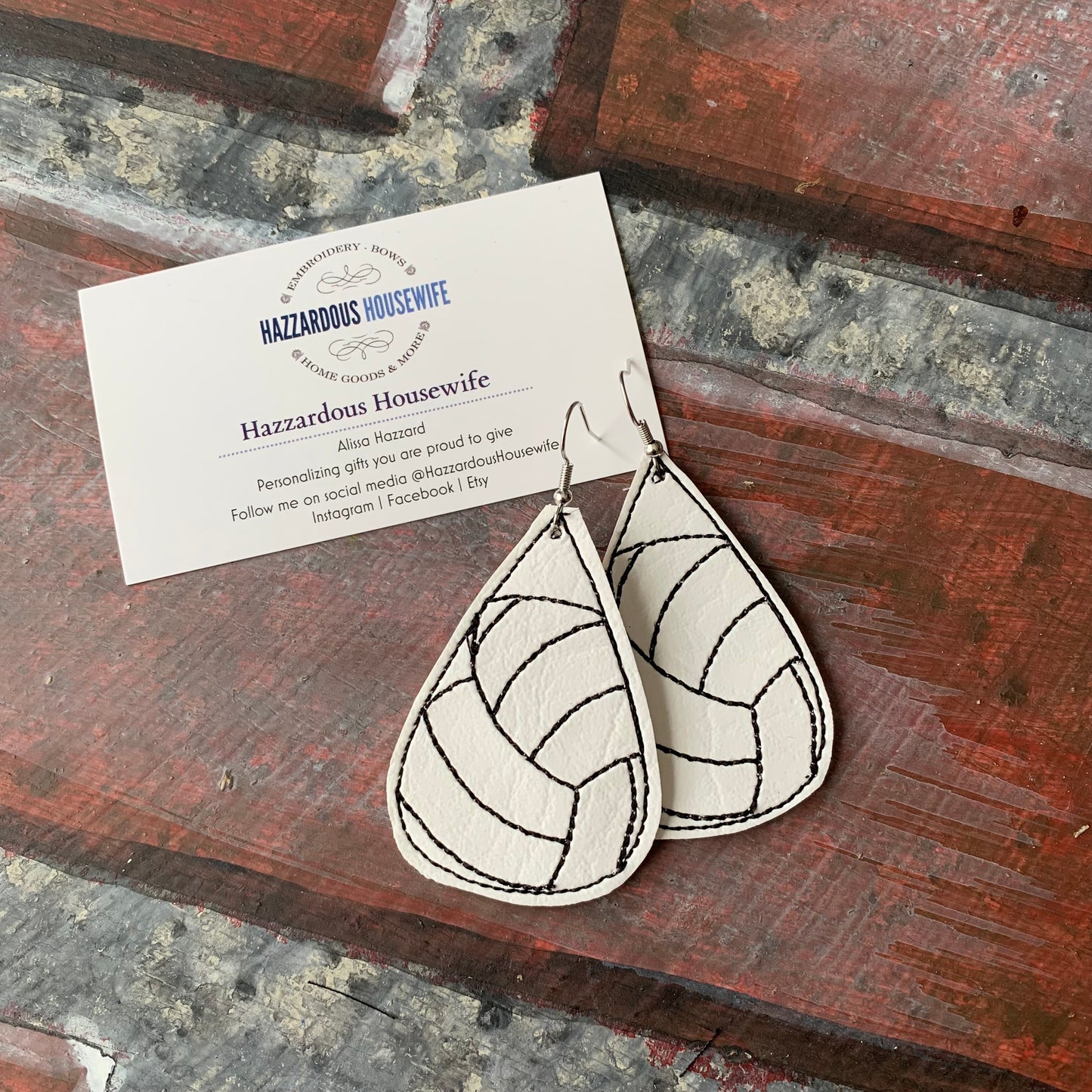 Teardrop-shaped volleyball earrings with geometric pattern on a wooden surface with a business card.