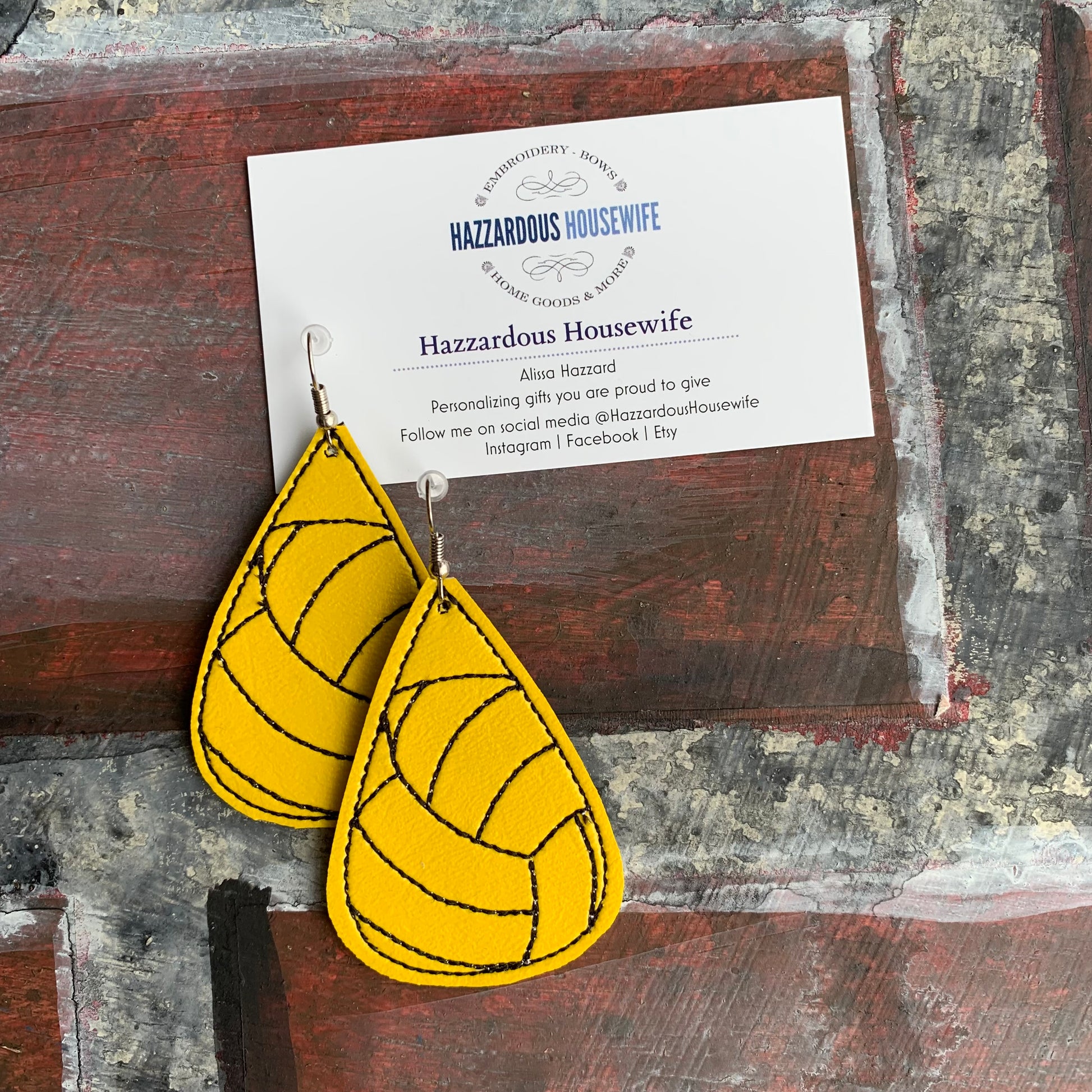 Yellow teardrop earrings on a rustic wooden surface with a branded card.