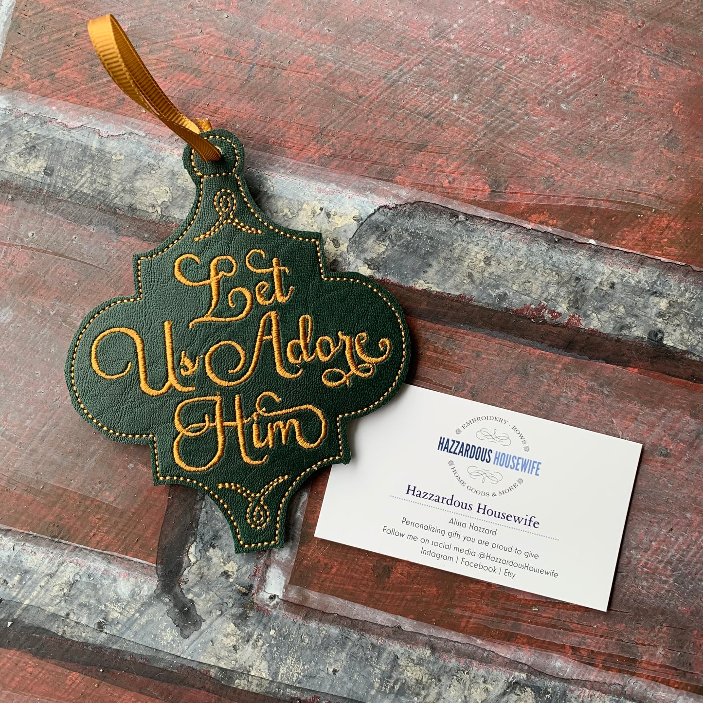 Decorative hanging sign with 'Let Us Adore Him' text on a wooden surface