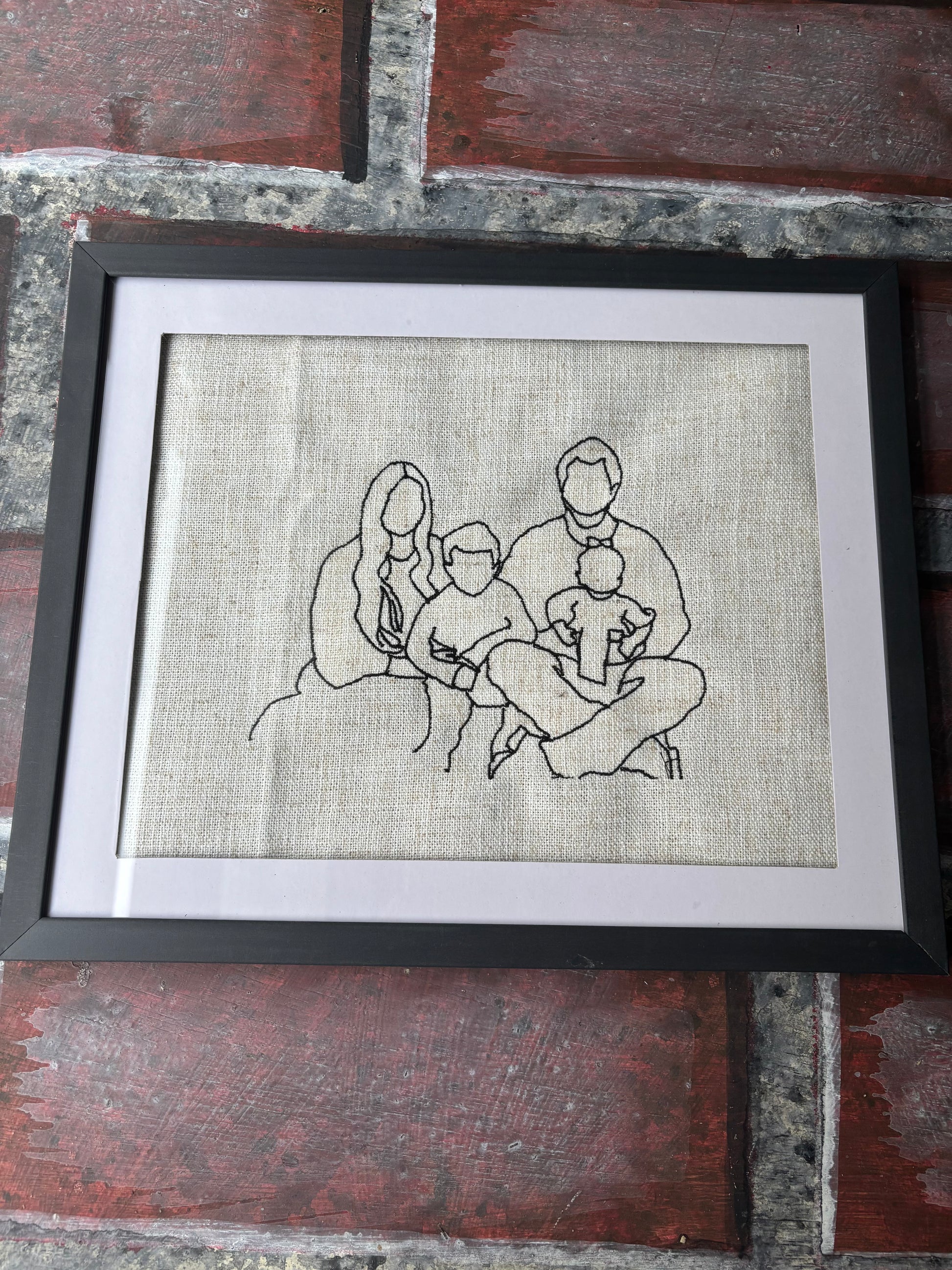 Framed black and white line drawing of a family on a textured fabric background