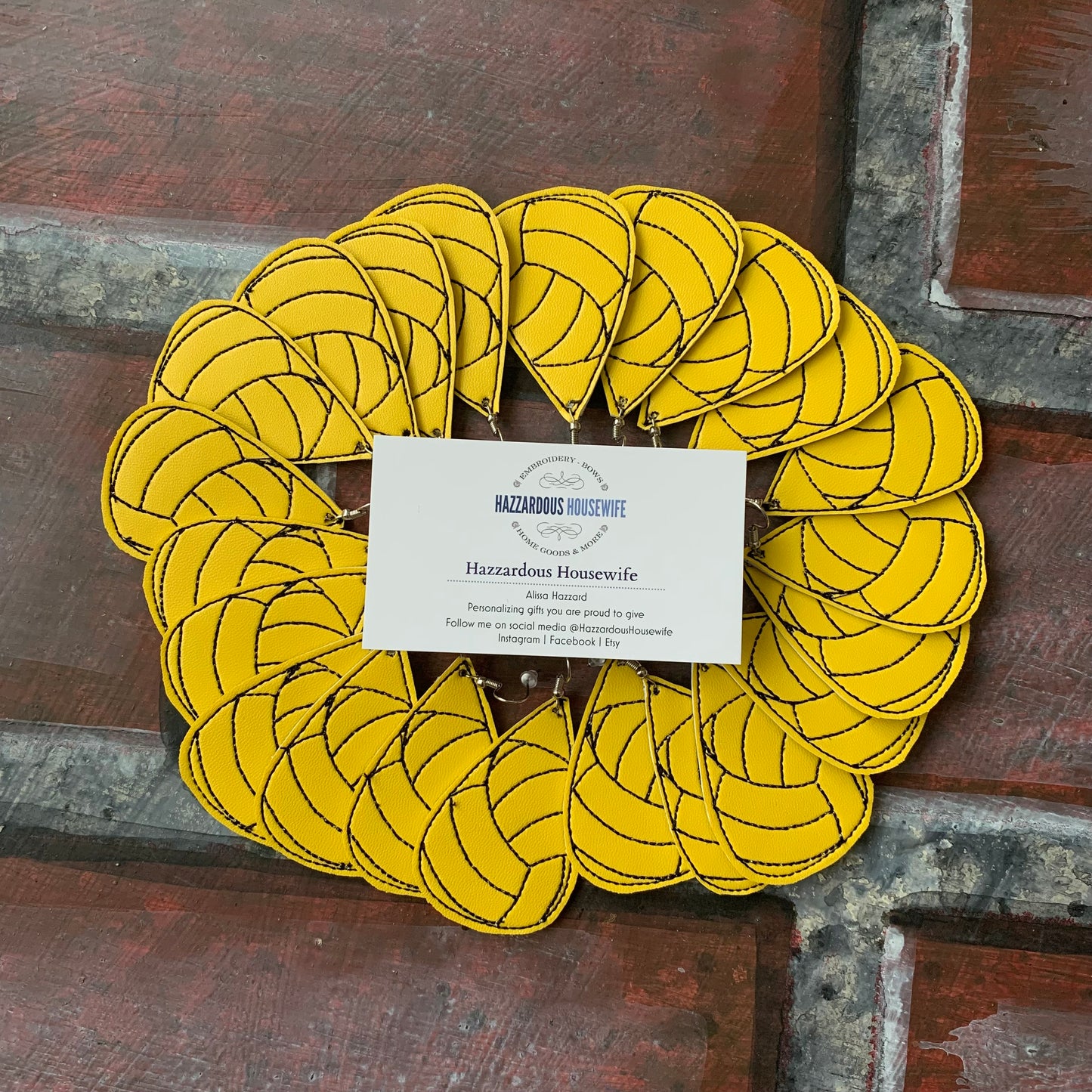 Multiple yellow water polo earrings styled in a wreath with a HazzardousHousewife business card in the center on a wooden background