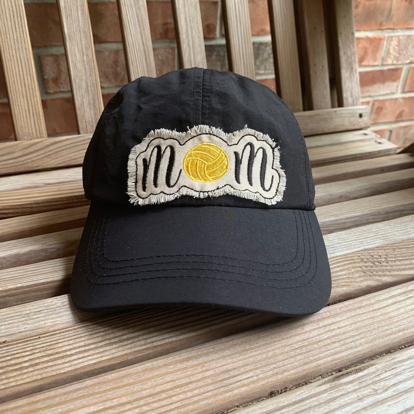 Black cap with 'mom' and water polo design on a wooden surface