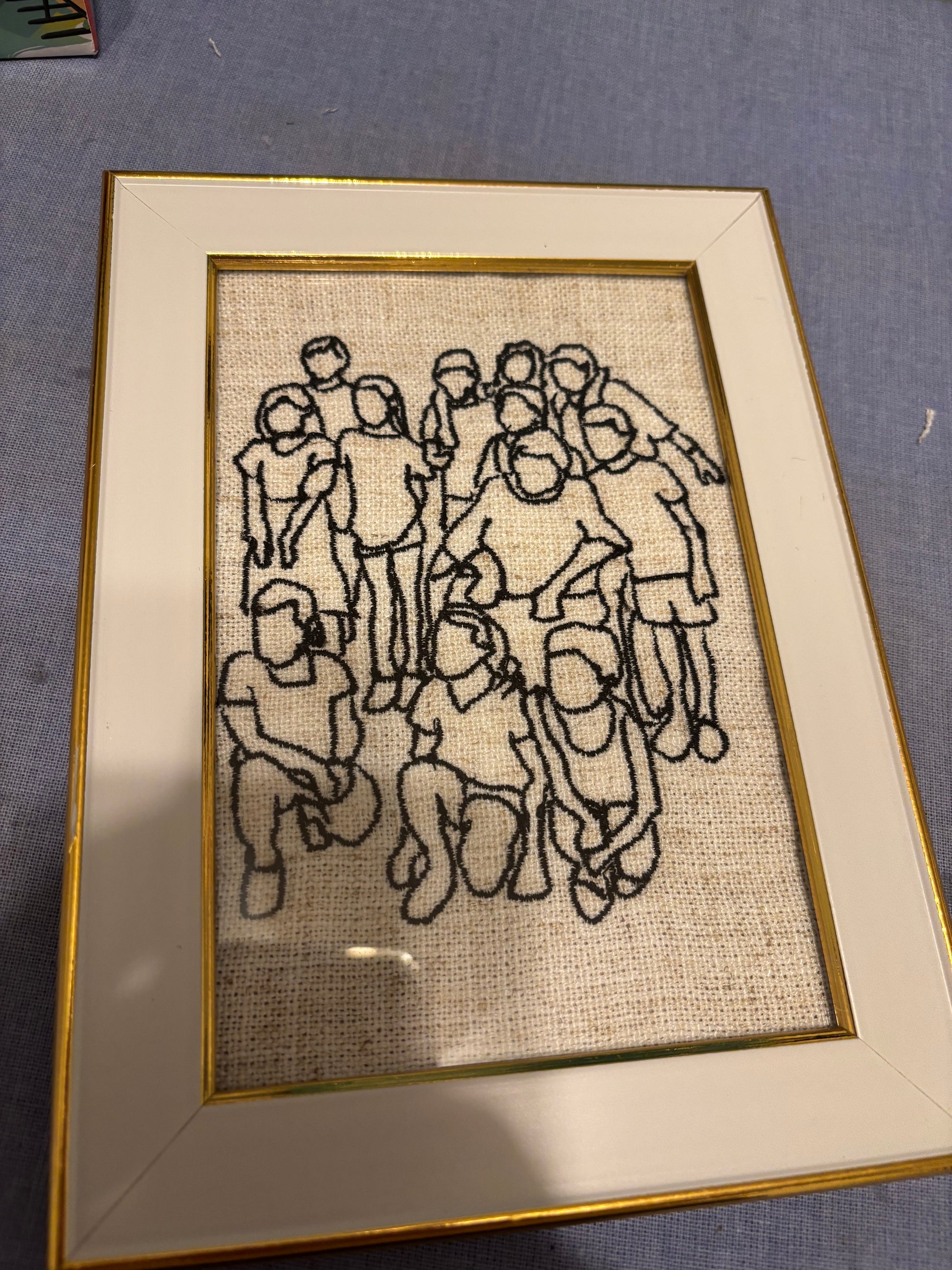 Framed needlepoint artwork of a group of people on fabric.