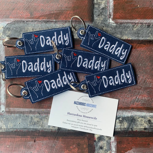 Set of 'Daddy' keychains on a wooden surface with a card below.