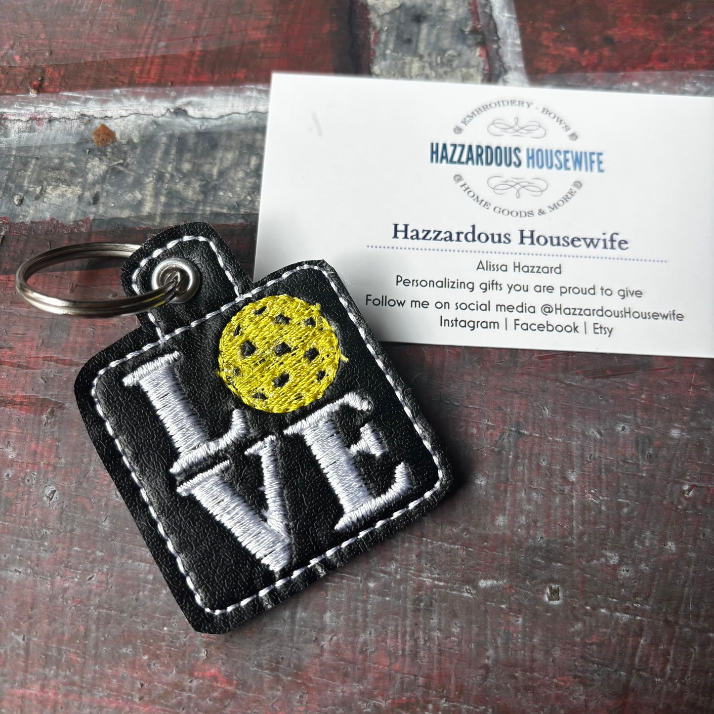 Pickleball Keychain with 'LOVE' embroidery and yellow pickleball circle on a card with 'Hazzardous Housewife' branding.