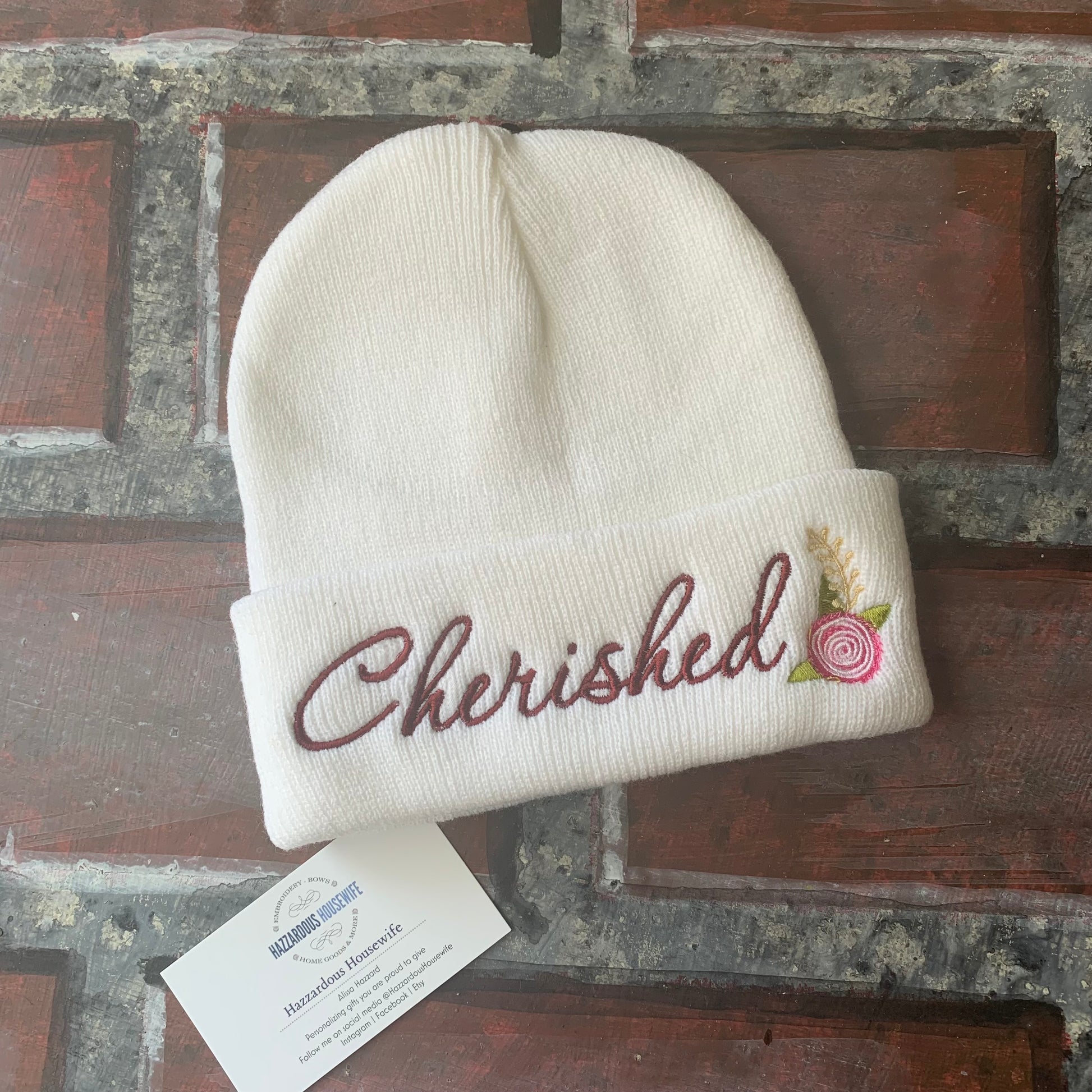 White beanie with 'Cherished' embroidery on a rustic wooden surface
