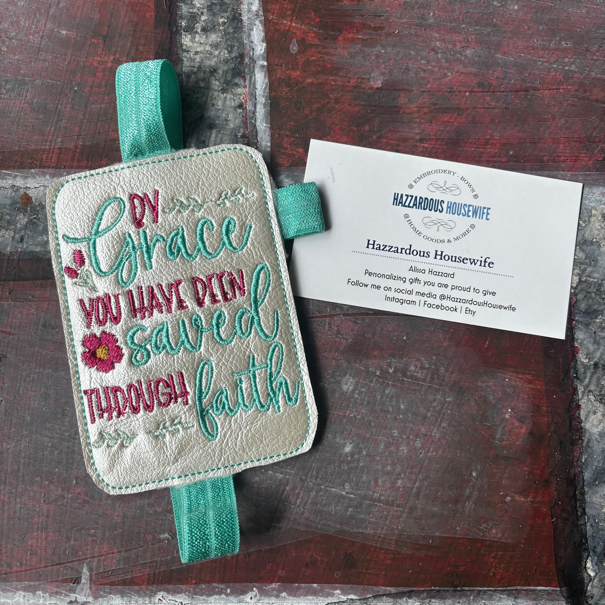 Embroidered book band with motivational quote on a wooden surface with a business card.