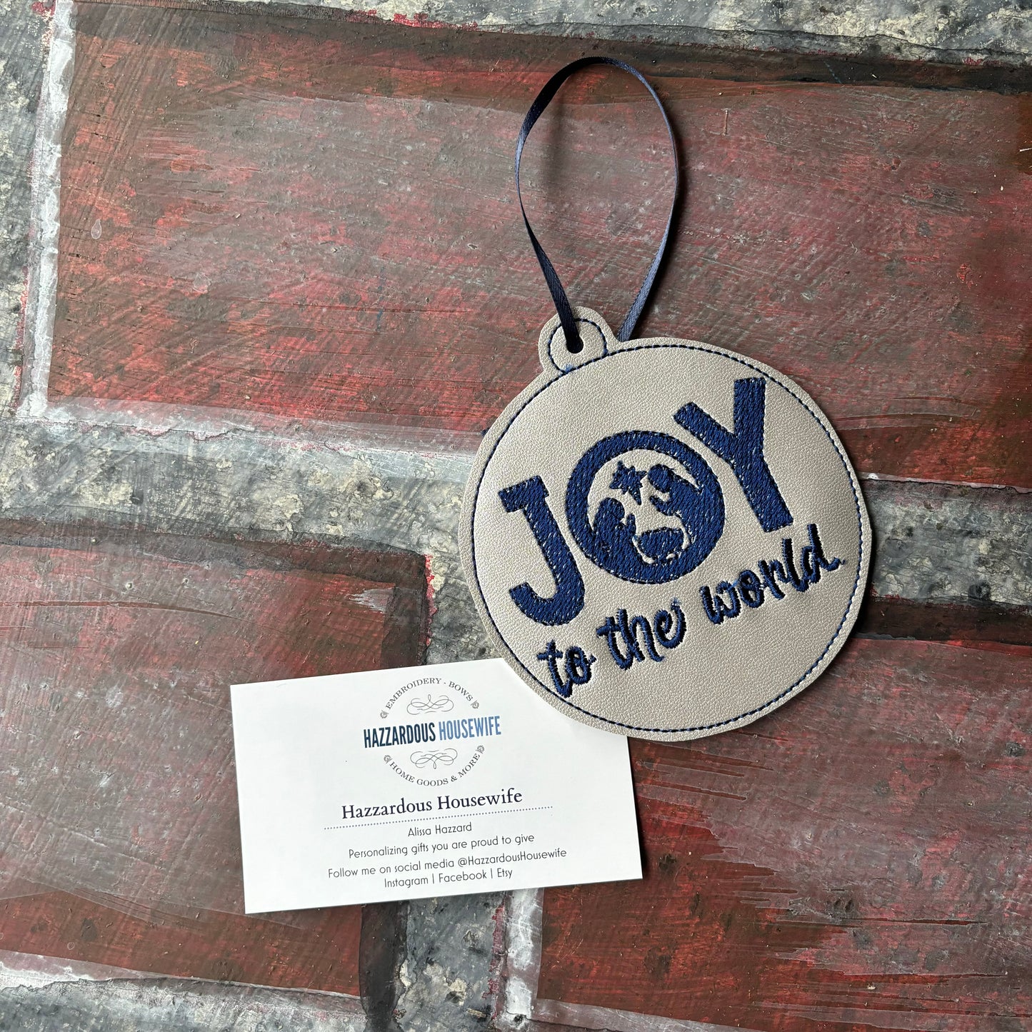 Round leather tag with 'Joy to the world' text on a wooden surface, featuring a card below.