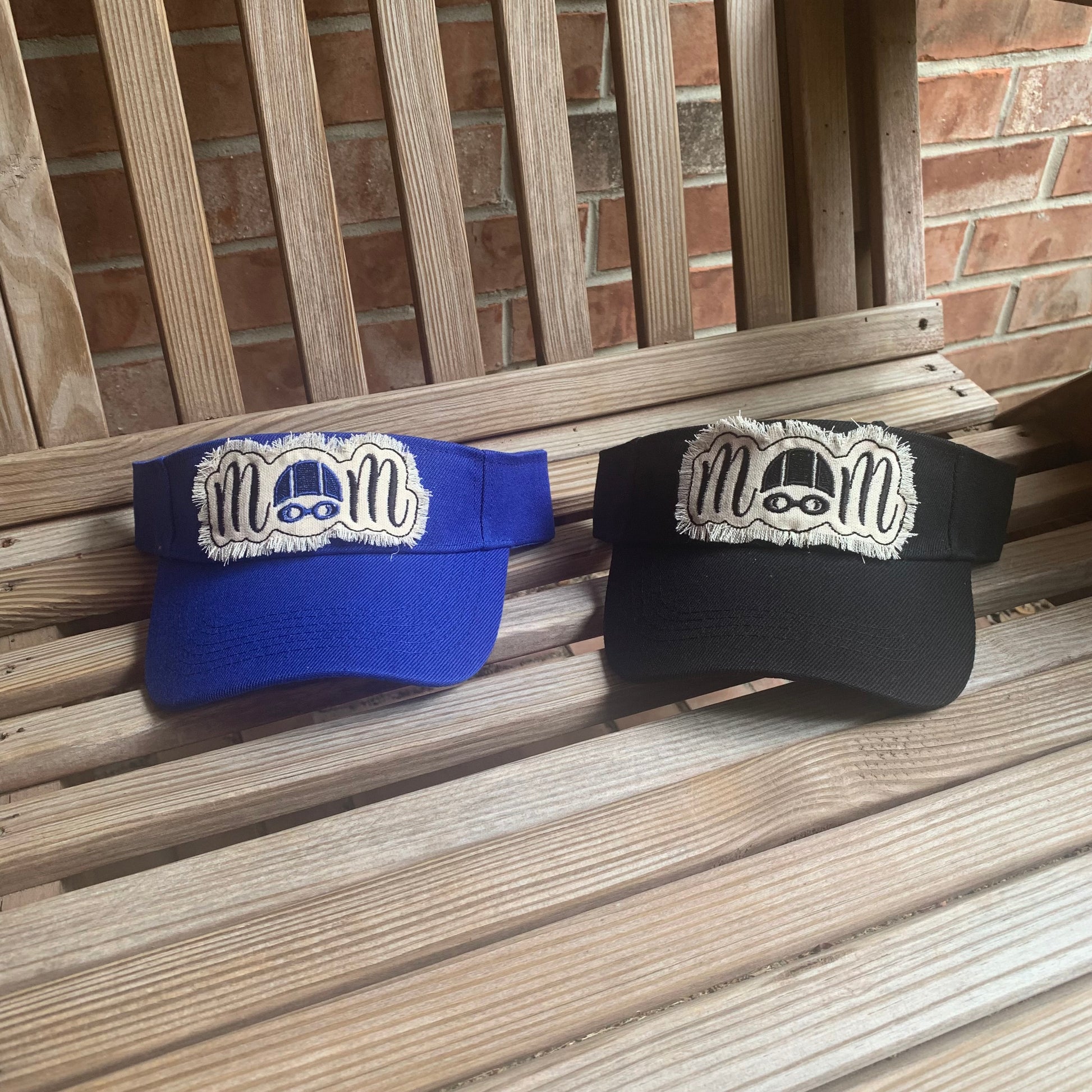 Two visors, one blue and one black, with a logo on a wooden surface.