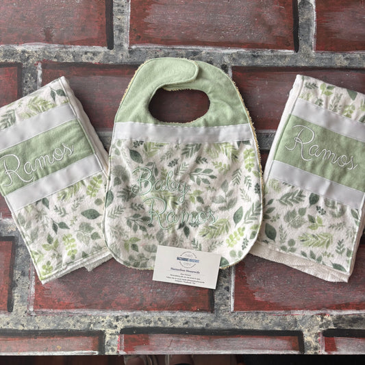 Set of nature green baby bib and burp cloths with personalized name branding on a brick surface.