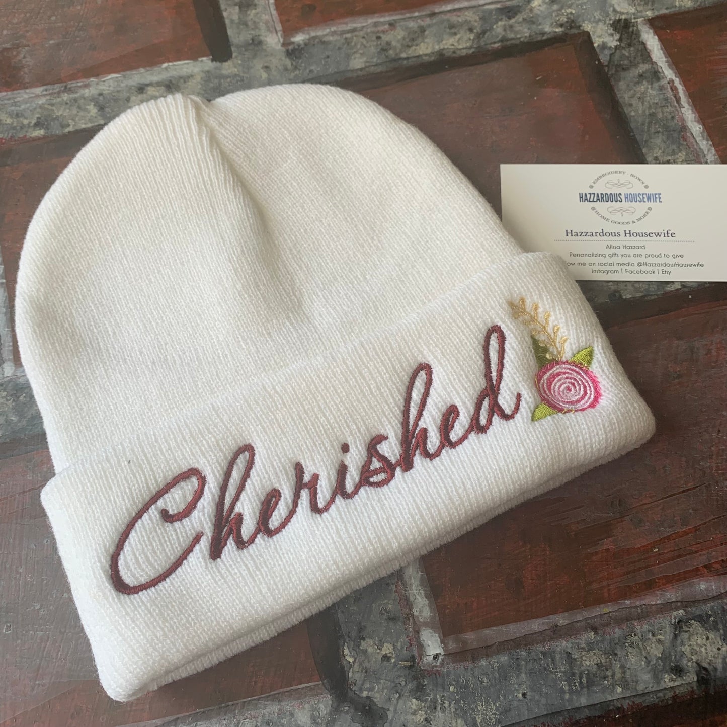 White beanie with 'Cherished' embroidery on a wooden surface