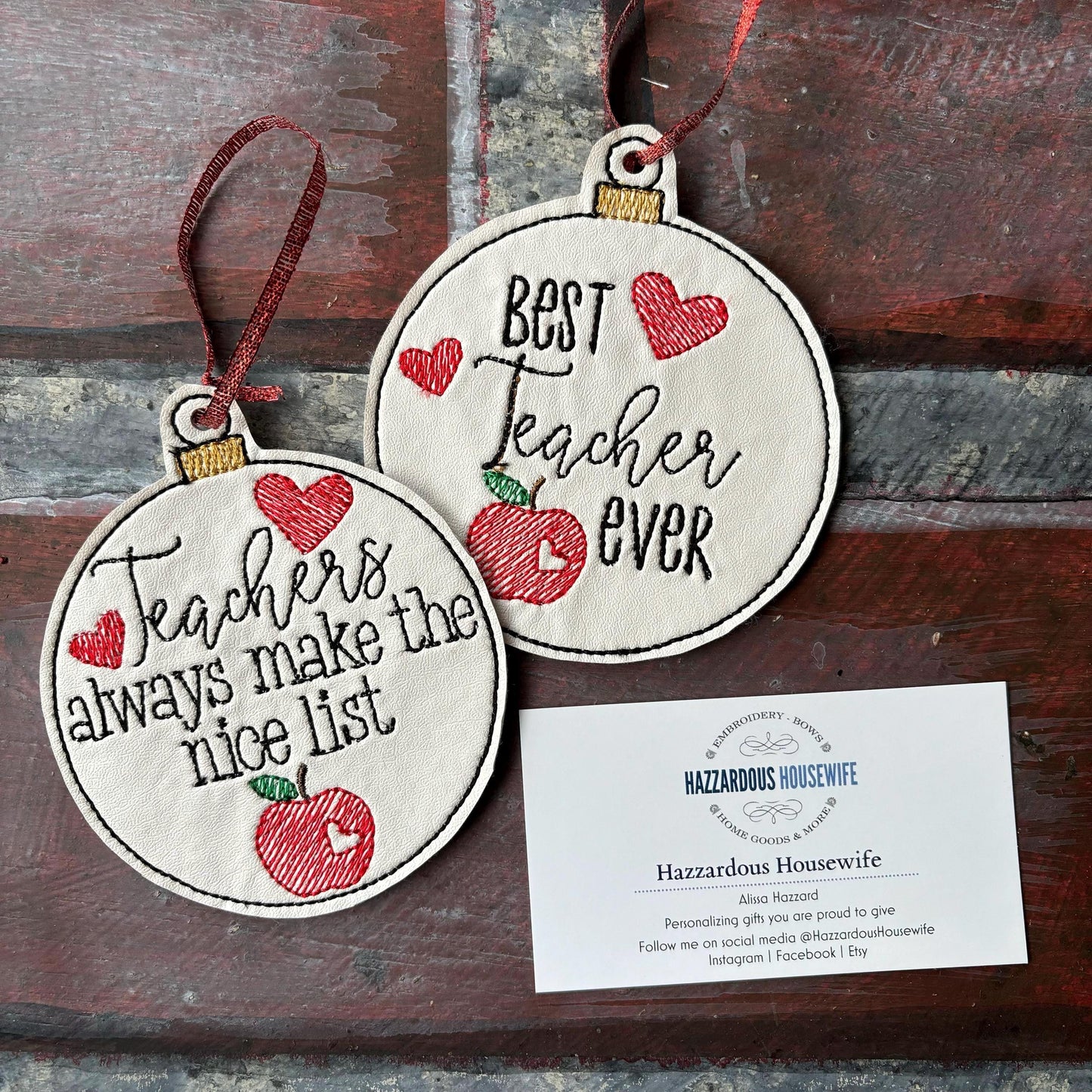 Two round embroidered ornaments with text and an apple design on a wooden surface, accompanied by a card.