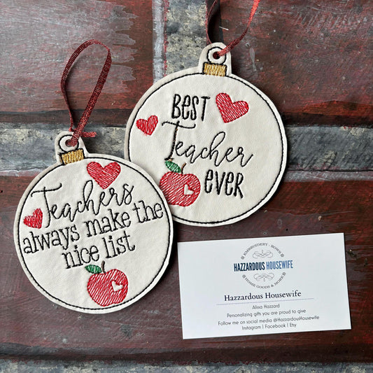 Two round embroidered ornaments with text and an apple design on a wooden surface, accompanied by a card.