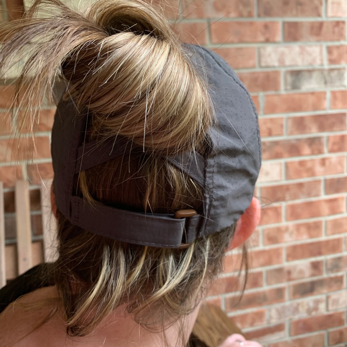 Person wearing a gray cap with crisscross straps and a gray band against a brick wall.