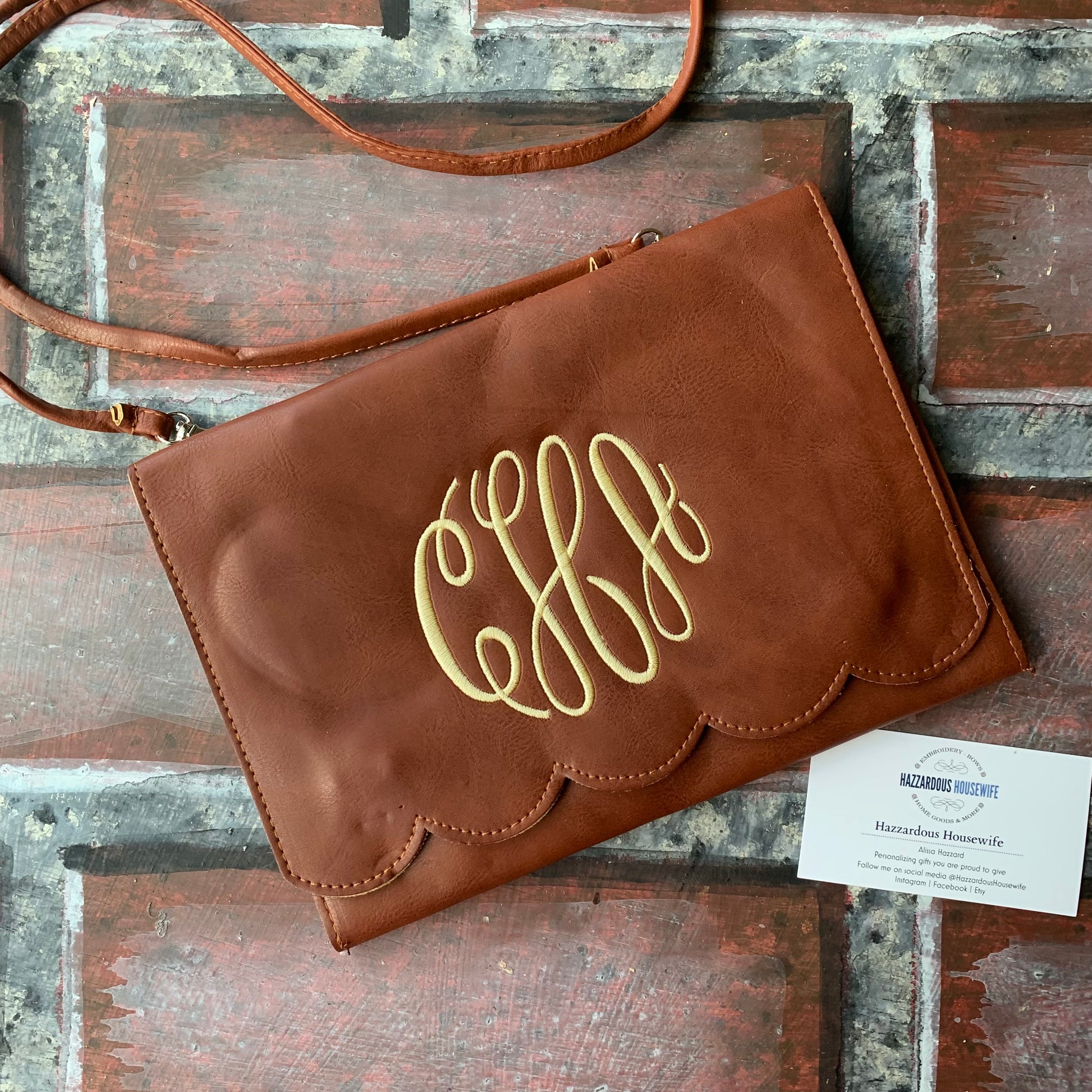 Brown leather clutch with gold monogram on a wooden surface
