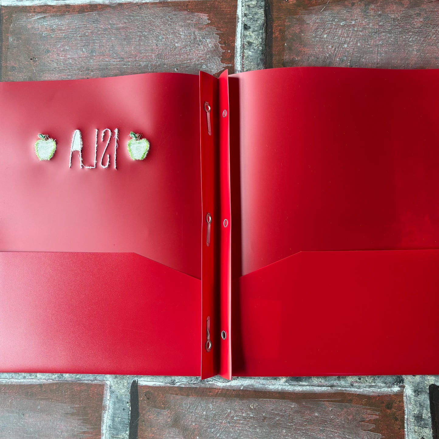 Red folder shown open with 3 brads and decorative elements on a wooden surface