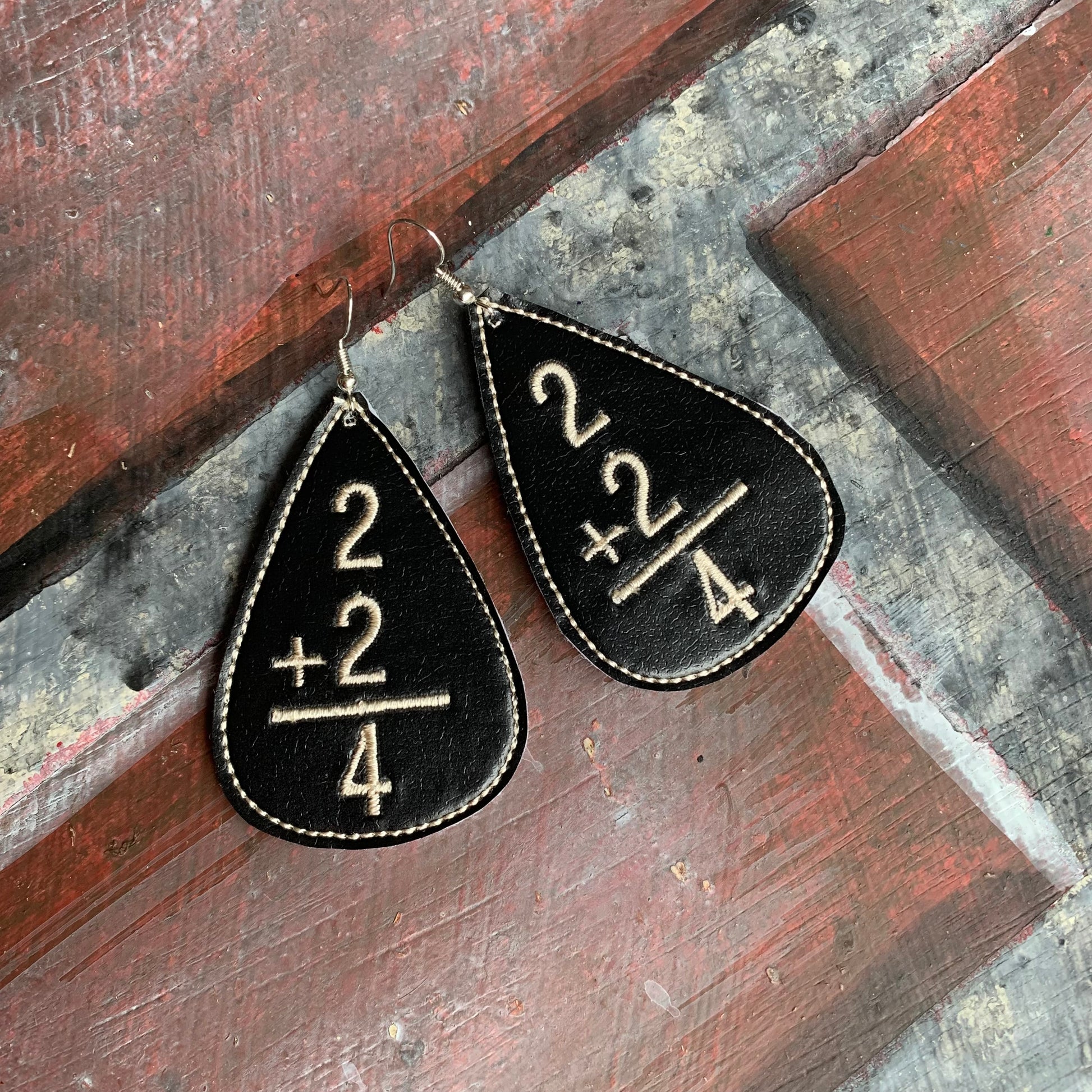 Black teardrop earrings with mathematical design on a rustic wooden surface