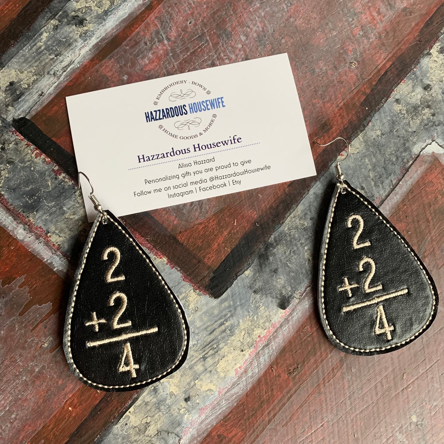 Black teardrop earrings with mathematical design on a wooden surface with a business card.