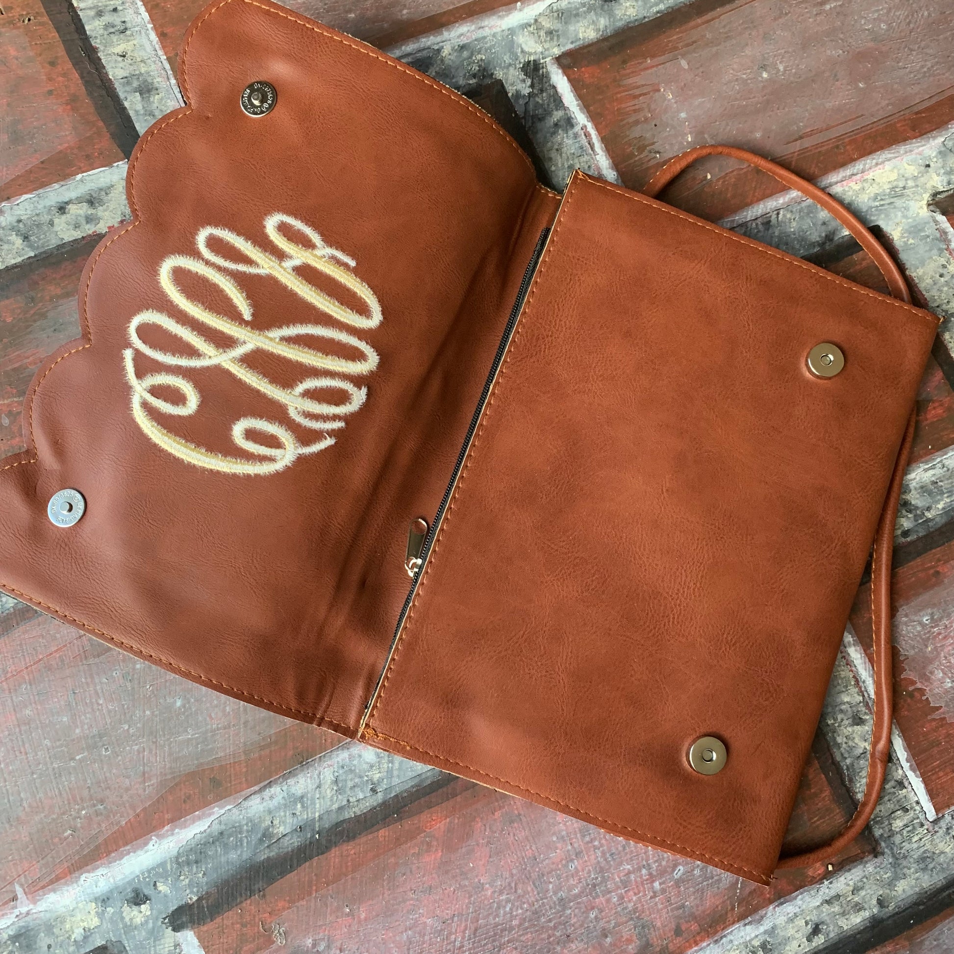 Brown leather purse with top flap flipped up to show inside surface with monogram on a textured surface