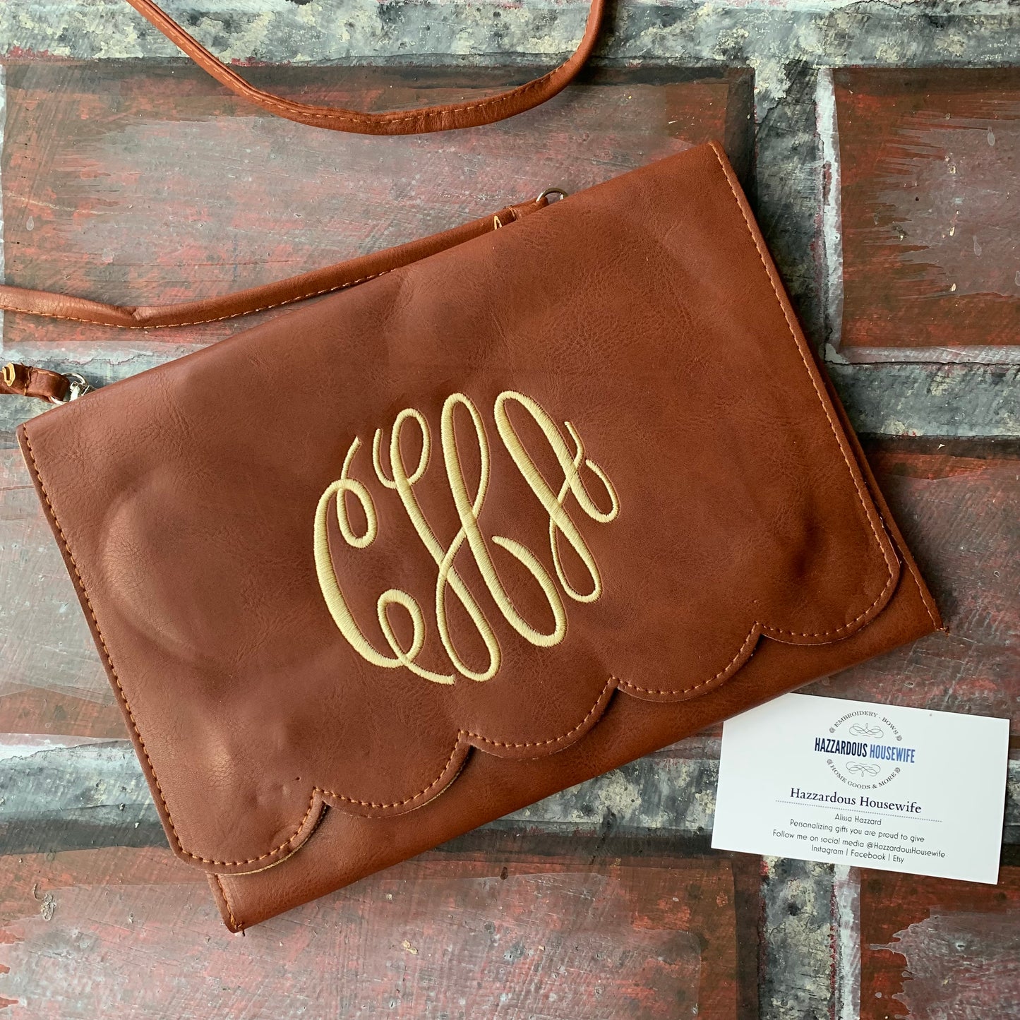 Brown leather clutch with gold monogram on a wooden surface