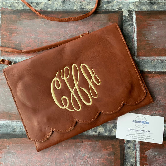 Brown leather clutch with gold monogram on a wooden surface