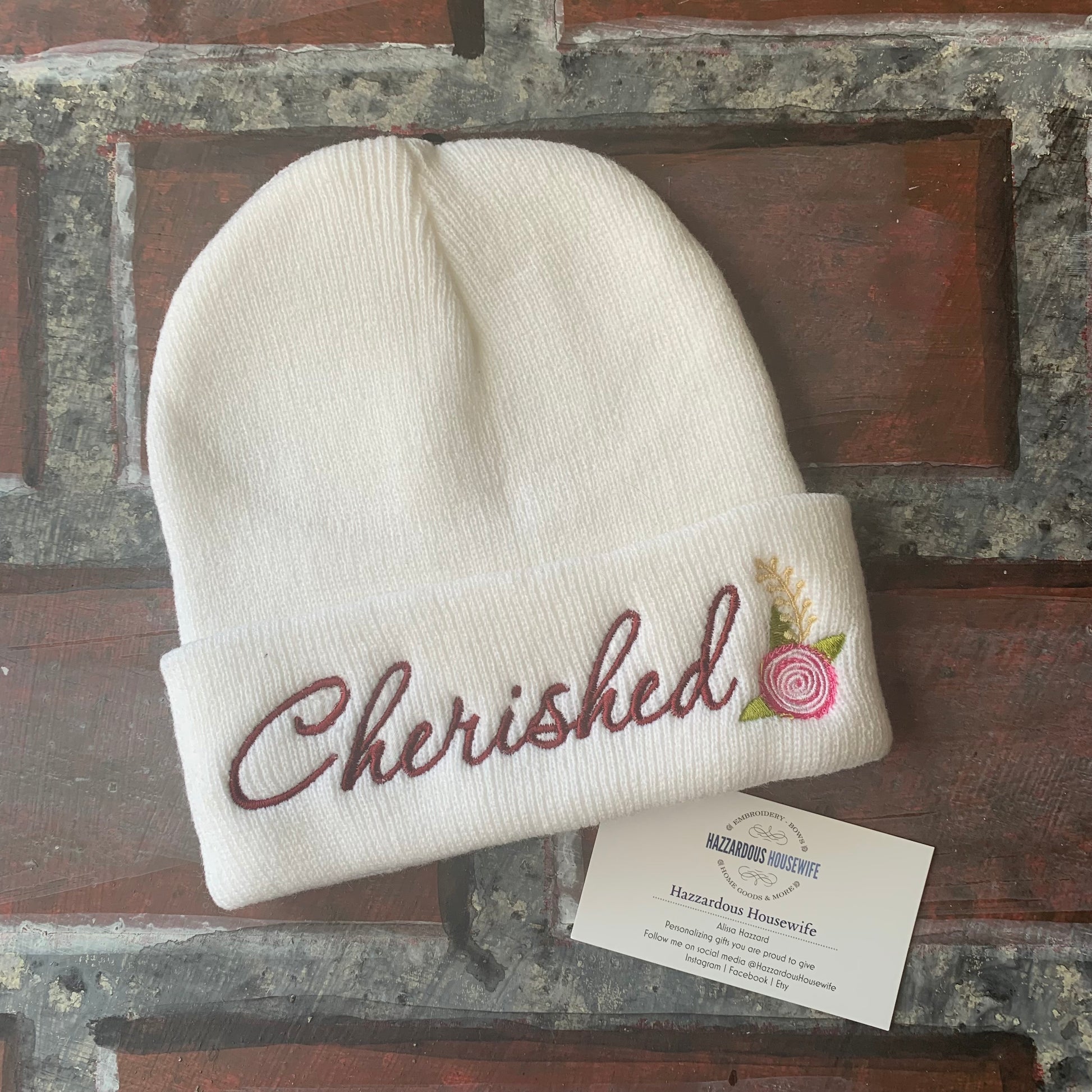 White beanie with 'Cherished' embroidery on a rustic wooden surface