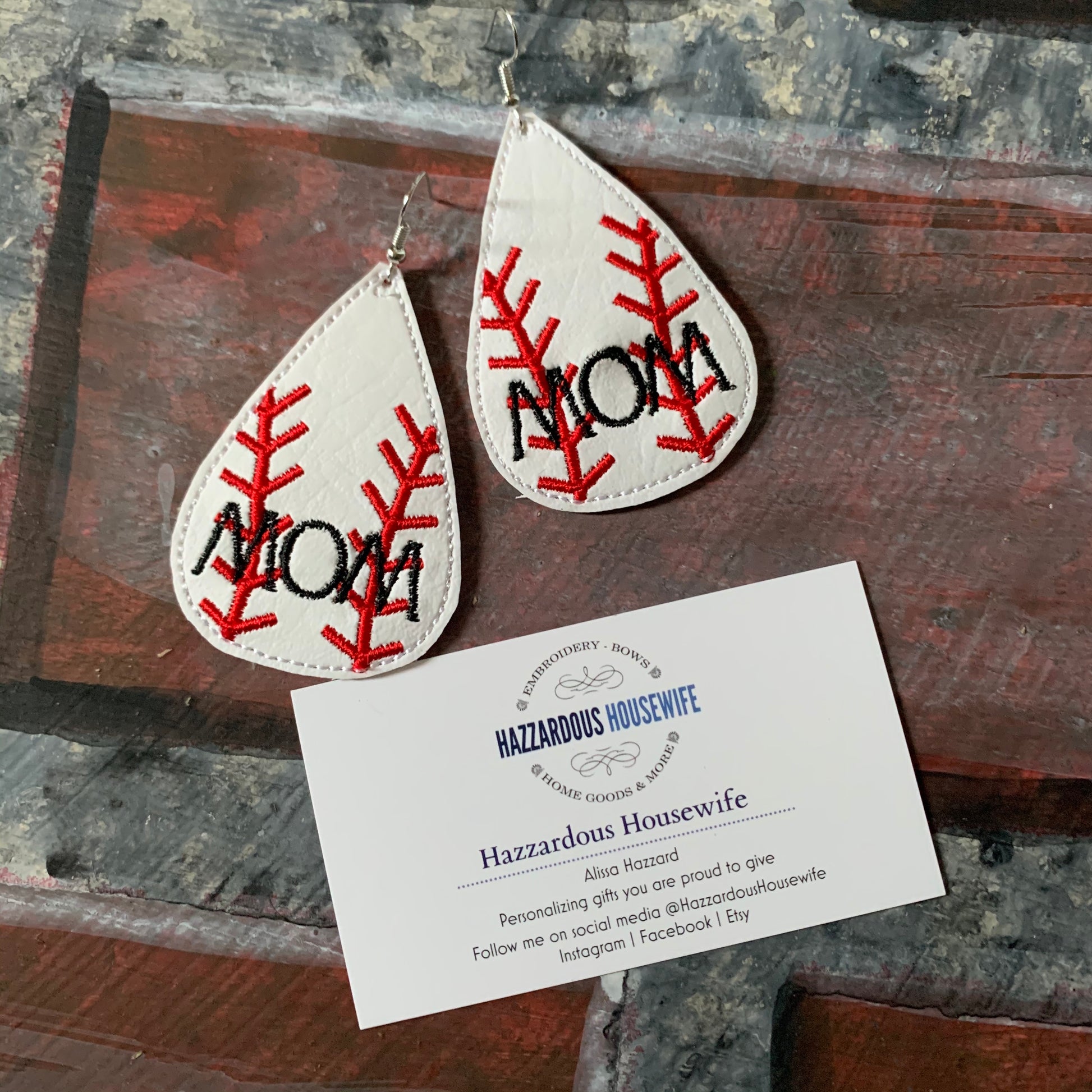 Teardrop-shaped earrings with 'MOM' embroidery on a wooden surface with a HazzardousHousewife business card.