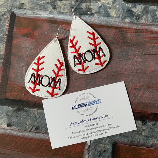 Teardrop-shaped earrings with 'MOM' embroidery on a wooden surface with a HazzardousHousewife business card.