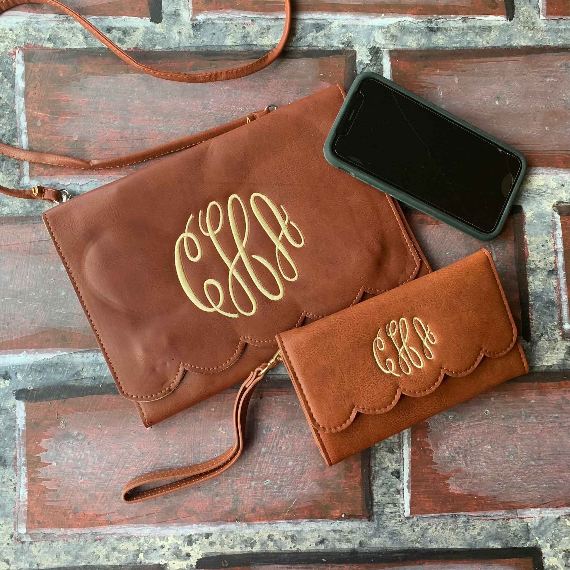 Brown clutch bag with gold monogram and matching wallet on a wooden surface
