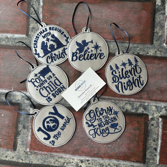 Set of Christmas-themed decorative silver and blue ornaments with text on a rustic wooden surface.