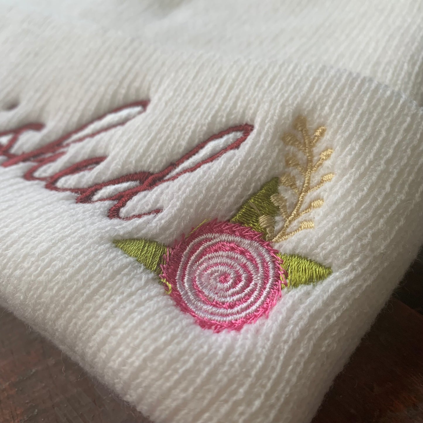 Embroidered floral design on a white fabric beanie with 'cherished' text.