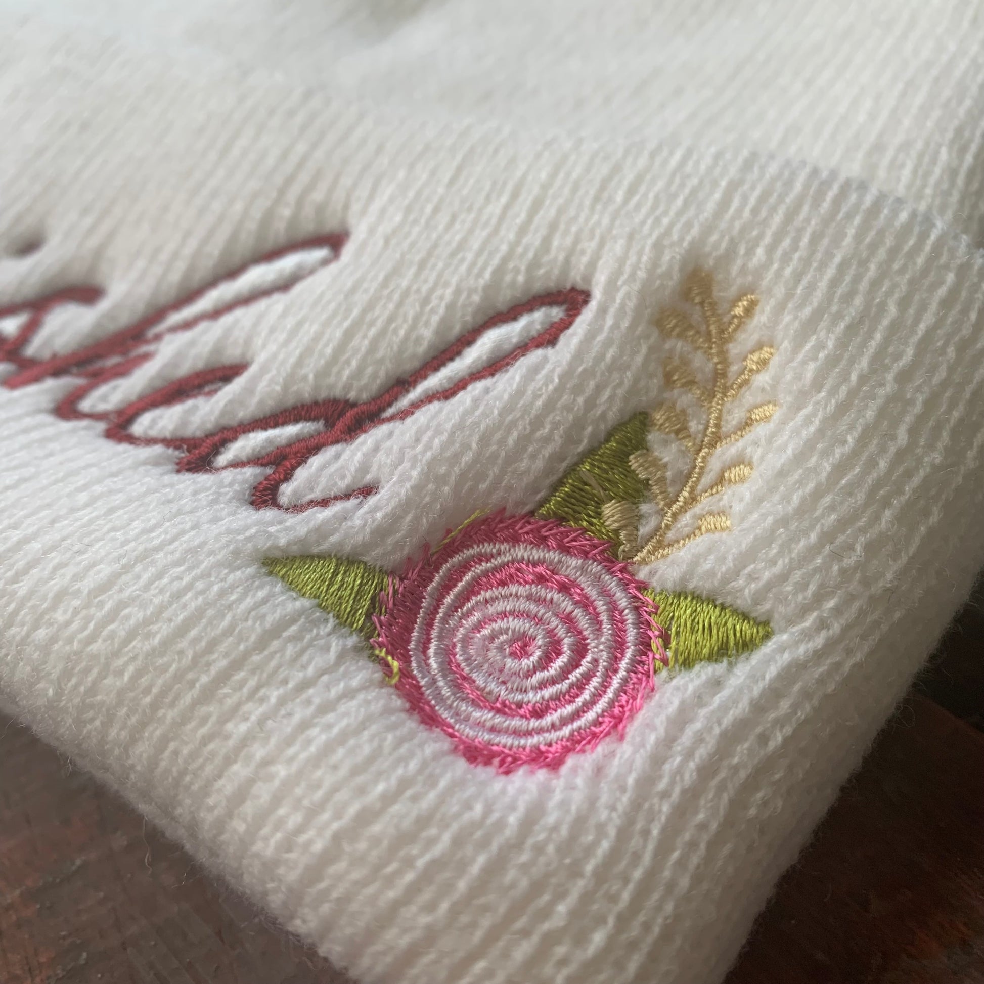 Embroidered floral design on a white fabric beanie with 'cherished' text.