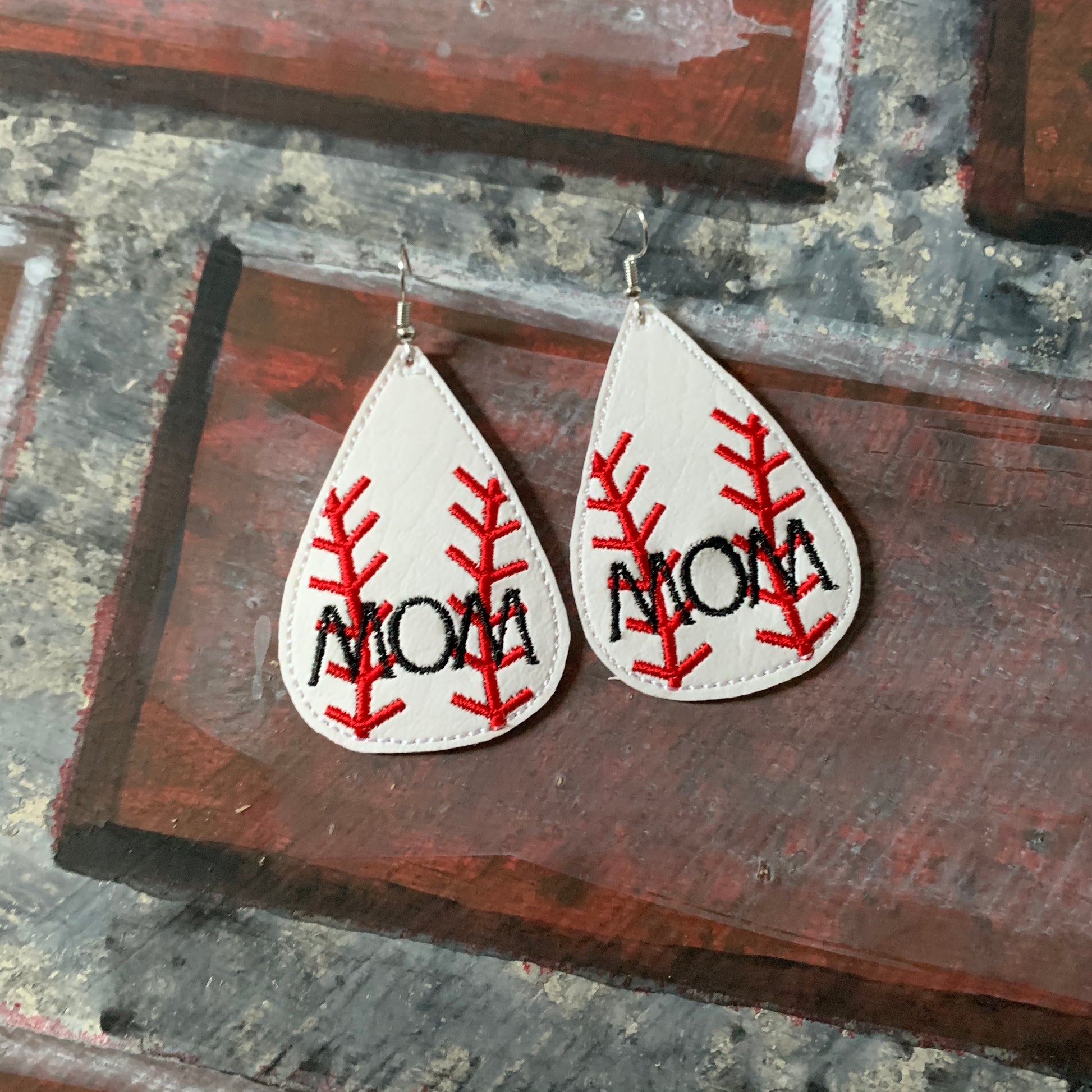 Teardrop-shaped earrings with 'MOM' and baseball design on a wooden surface