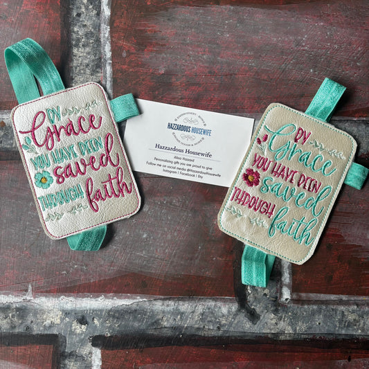 Two embroidered book bands with text and ribbons on a wooden surface