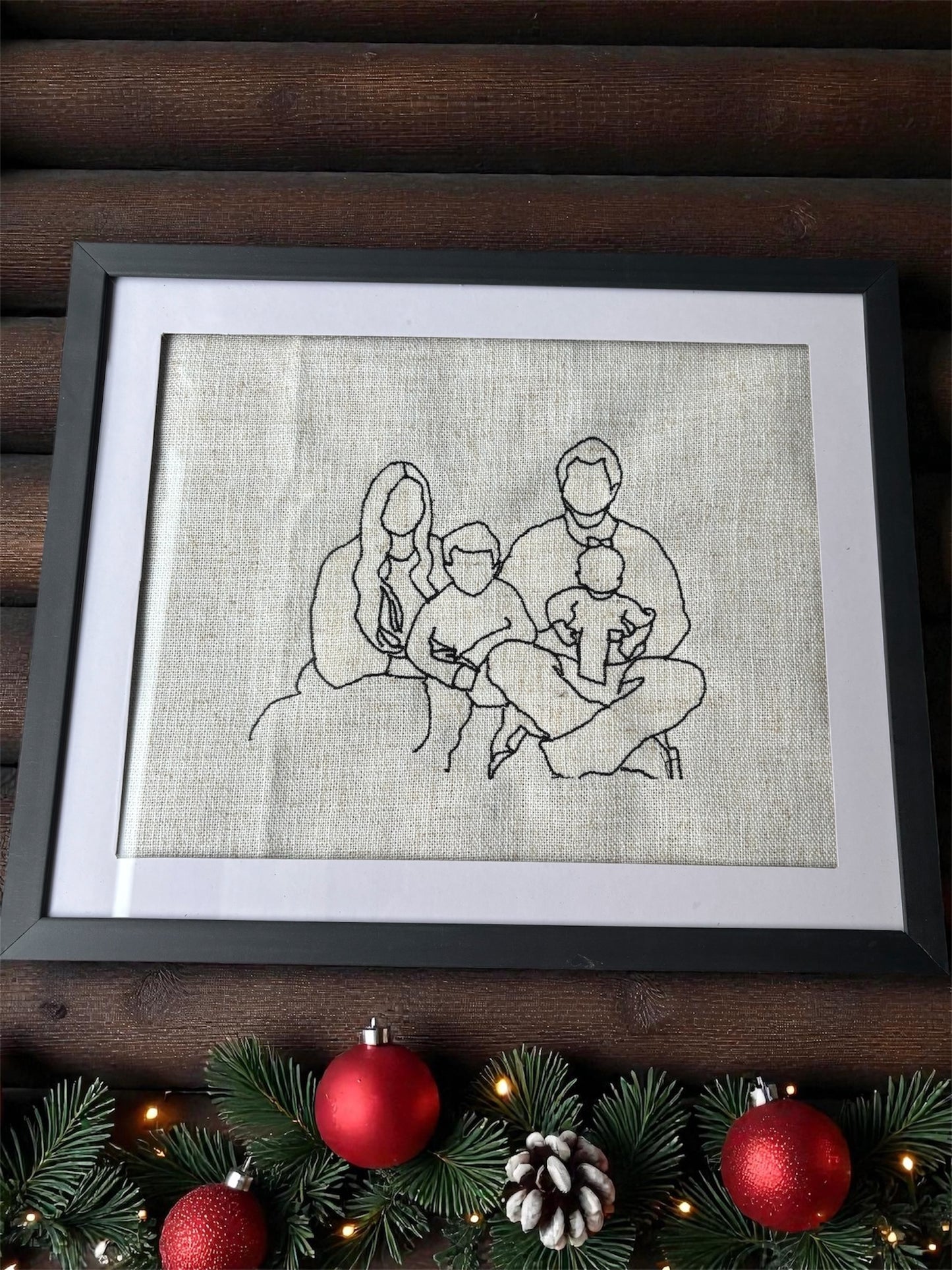 Framed embroidered artwork of a family sitting together on a wooden surface with Christmas decorations.