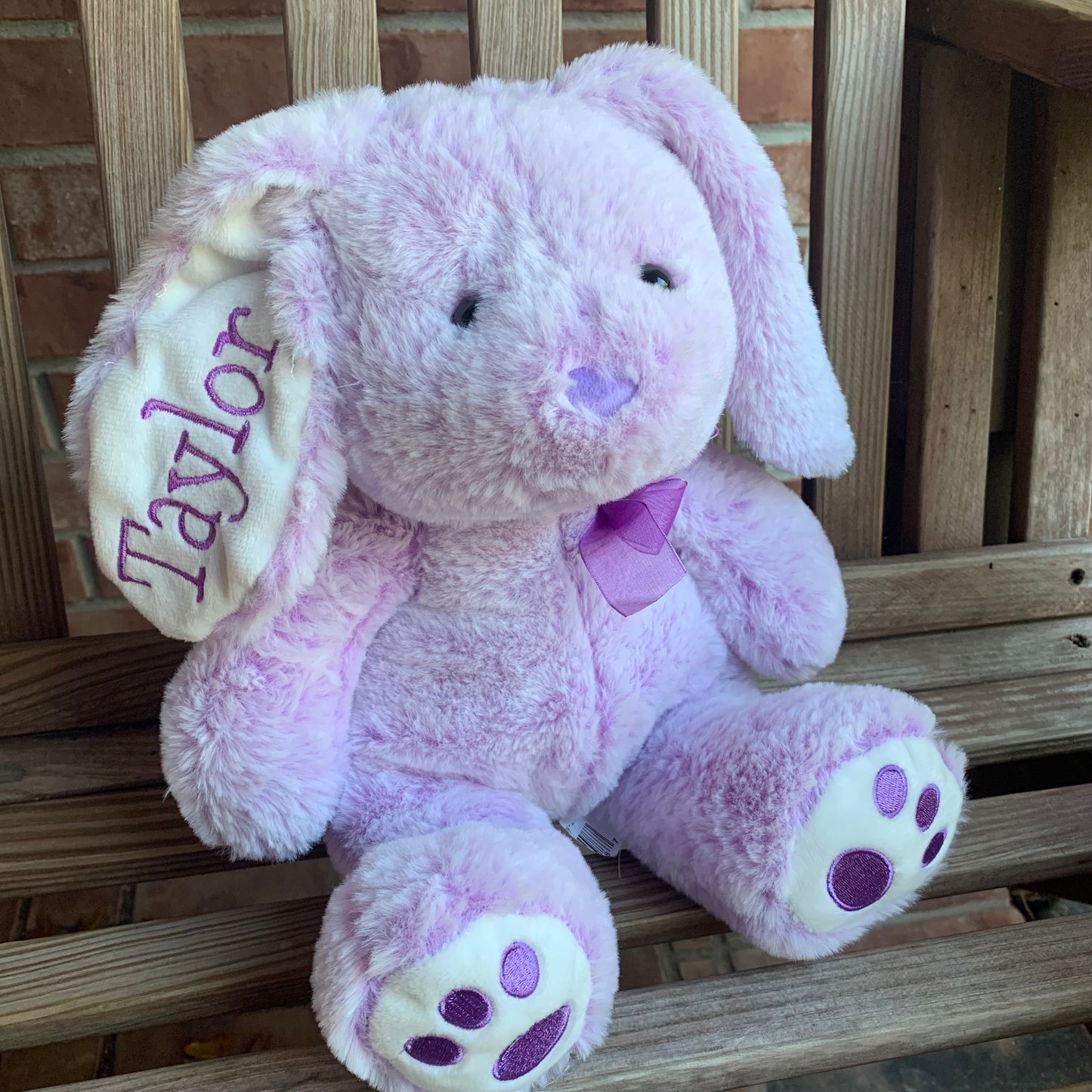 Purple teddy bunny with 'Taylor' on an ear, sitting on a wooden surface.