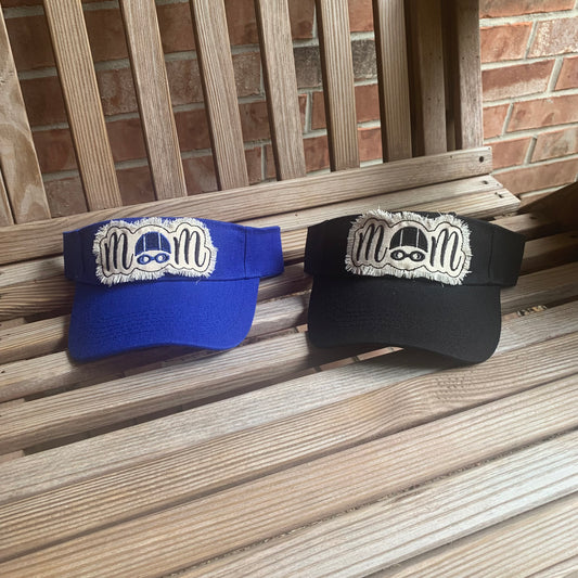 Two visors, one blue and one black, with a swim mom logo on a wooden surface.