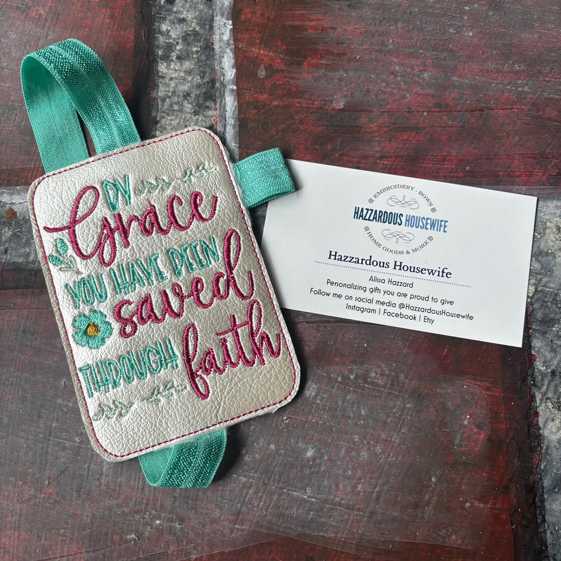 Embroidered bookmark with quote that says "by Grace you have been saved through faith" on a wooden surface