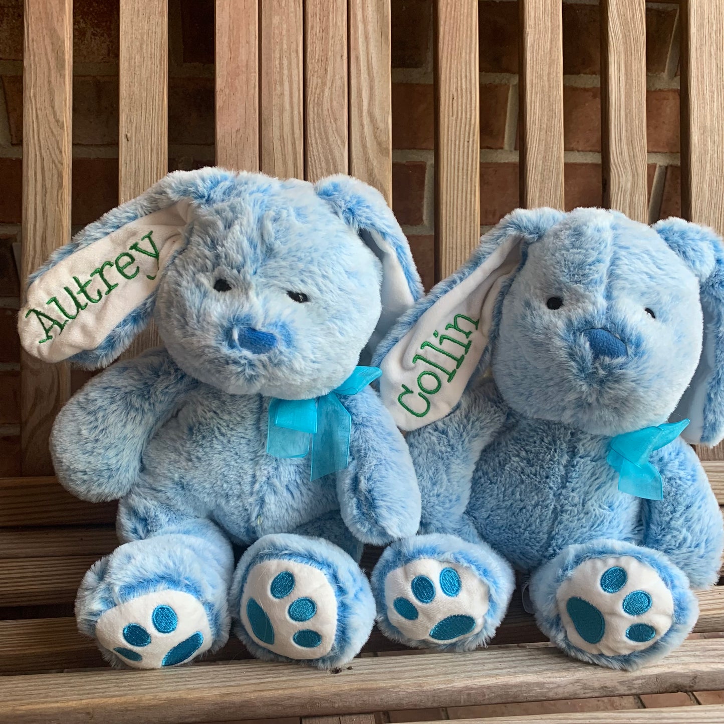 Two blue plush Easter bunnies with name embroidered on ear on a wooden surface