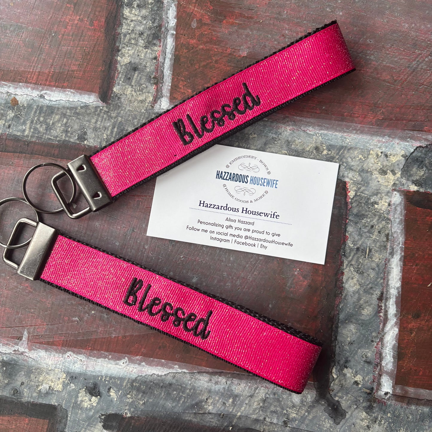 Pink keychain with 'Blessed' text in black on a rustic surface with a business card.