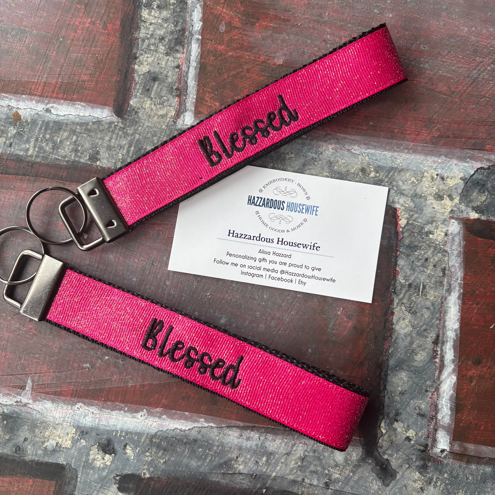 Pink keychain with 'Blessed' text in black on a rustic surface with a business card.